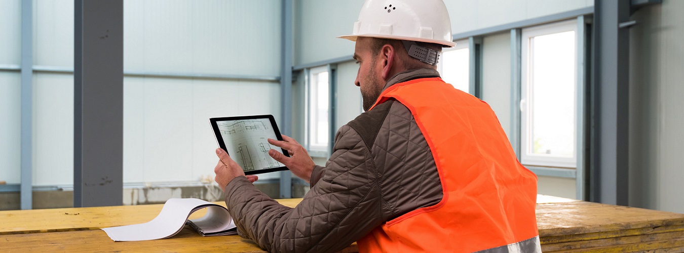 Construction supervisor checks the interior of a new warehouse being constructed with digital tablets in his hand, wearing a safety helmet and vest